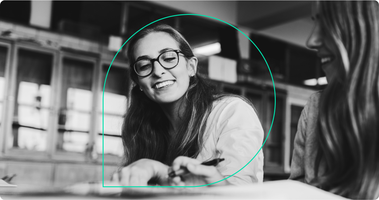 A person wearing glasses smiles at a desk behind an outline of the Grammarly logo