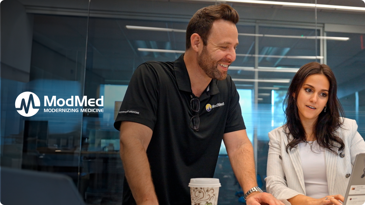 Two smiling ModMed employees work at a desk