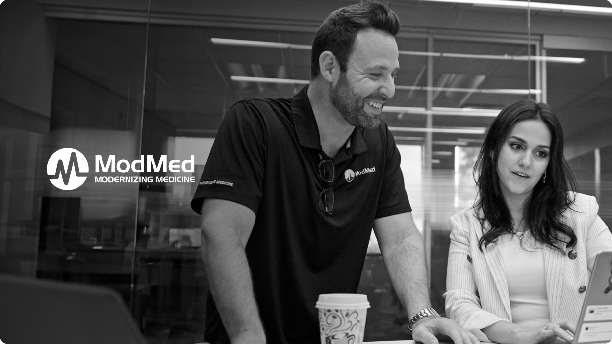 Two smiling ModMed employees work at a desk