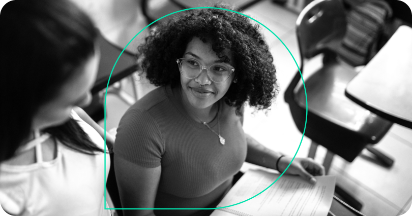 A student smiles while sitting at a desk in a classroom