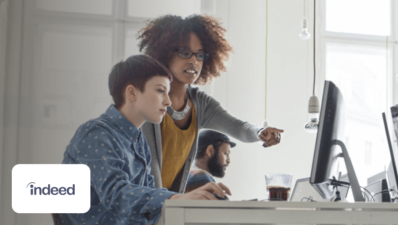 Two women looking at a computer behind the Indeed logo