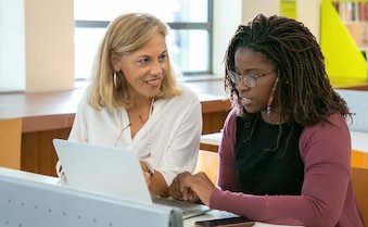 Two smiling colleagues talk at a desk.