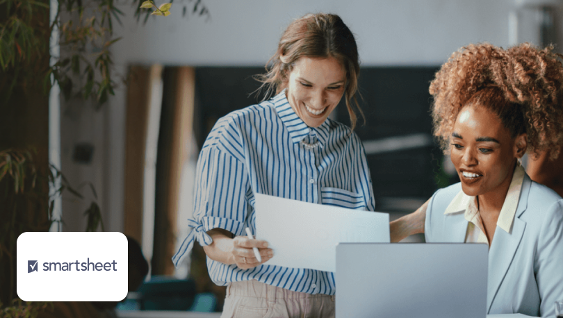 Two women looking at a paper document beside the Smartsheet logo